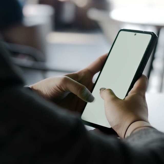 A person holds a smartphone in a café, suggesting studying on the go.
